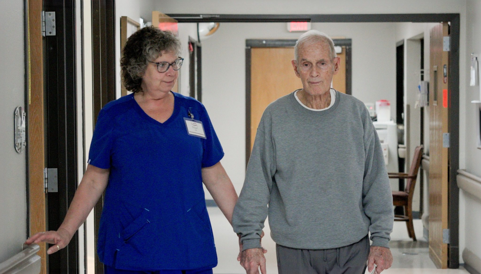 A nurse walking a resident at Care Manor, a skilled nursing facility and nursing home, down a hallway