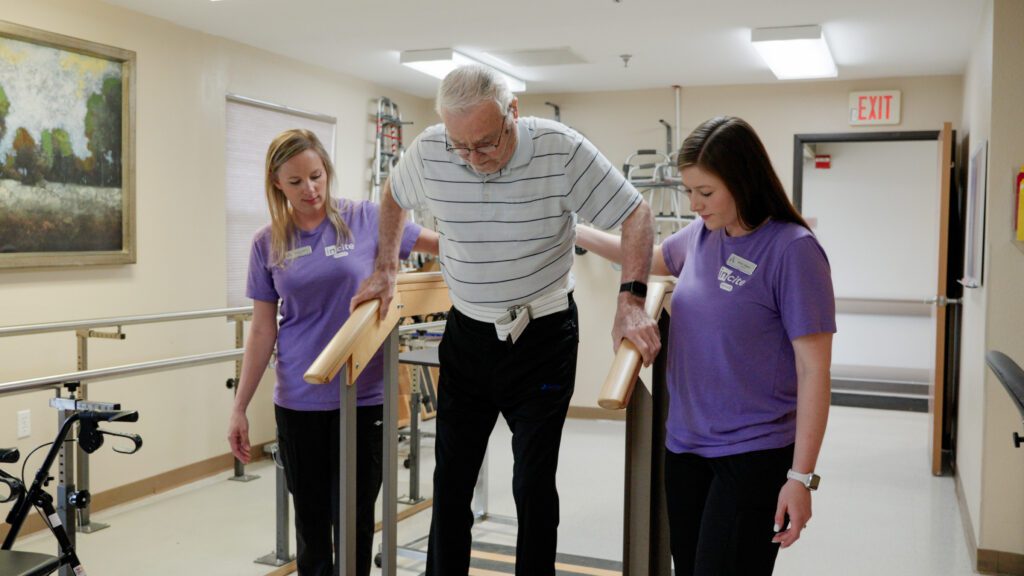 A man and two nurses helping him with therapy at a short term rehab facility